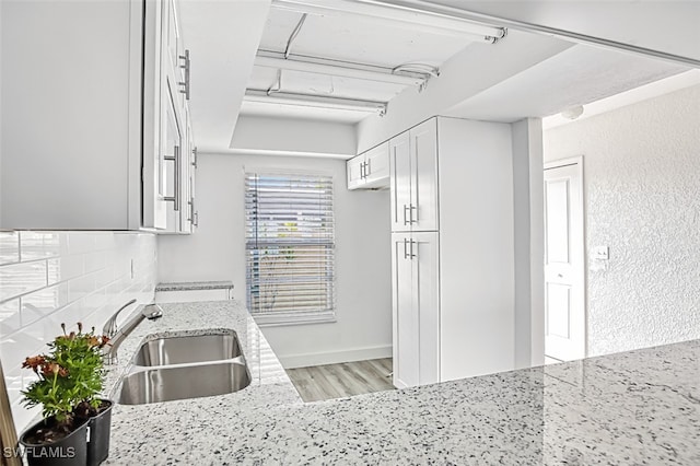 kitchen with light stone countertops, sink, white cabinetry, and light wood-type flooring