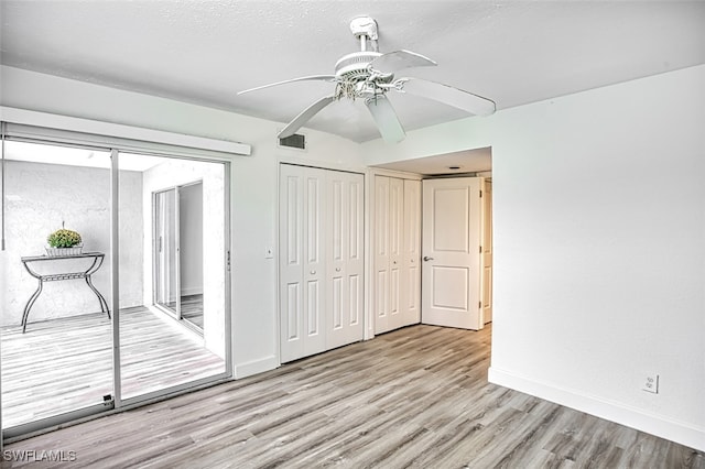 unfurnished bedroom featuring ceiling fan, light hardwood / wood-style flooring, and two closets