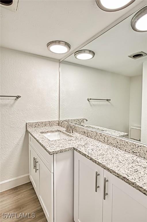 bathroom featuring visible vents, wood finished floors, baseboards, vanity, and a textured wall