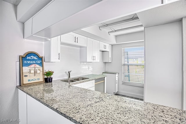 kitchen featuring a sink, stone countertops, backsplash, and white cabinetry