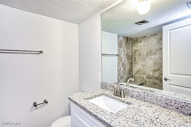 bathroom featuring vanity, a textured wall, toilet, and a textured ceiling