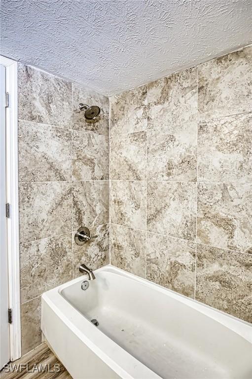 full bathroom featuring shower / bath combination, a textured ceiling, and tile walls