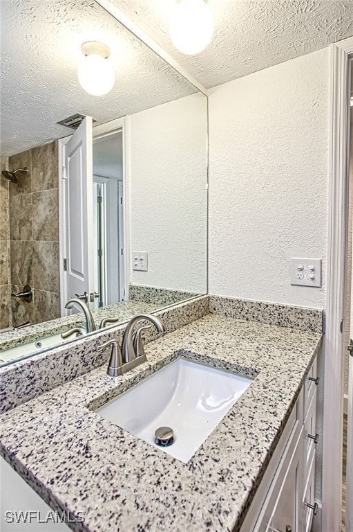 bathroom featuring vanity, a tile shower, and a textured ceiling