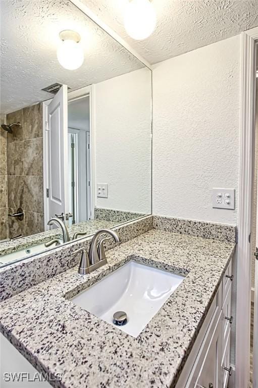bathroom with vanity, a textured wall, a tile shower, and a textured ceiling