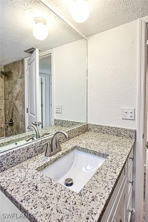 16251 Dublin Cir Unit F104, Fort Myers, FL 33908 - bathroom with vanity, a textured wall, a tile shower, and a textured ceiling