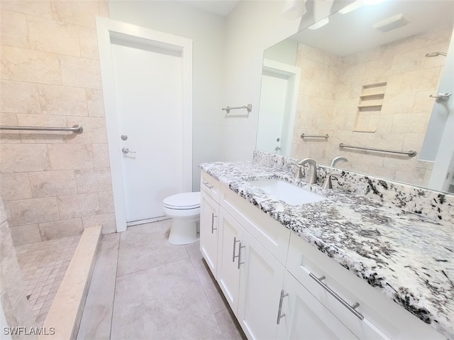 bathroom with a tile shower, vanity, tile patterned floors, and toilet