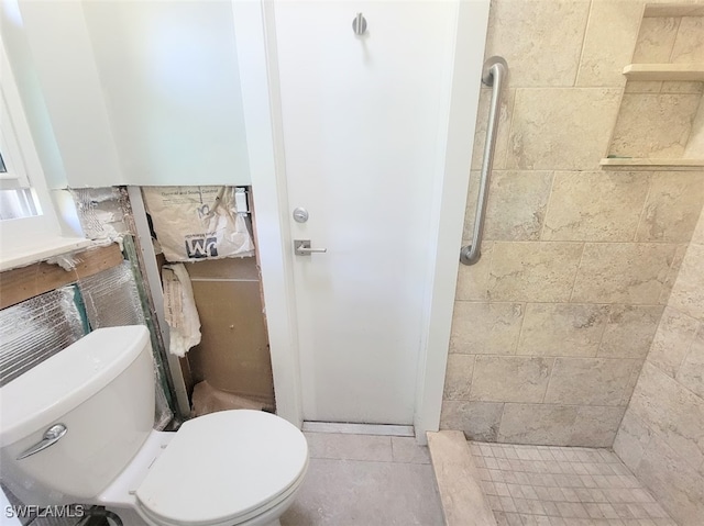 bathroom featuring tile patterned flooring, tiled shower, and toilet