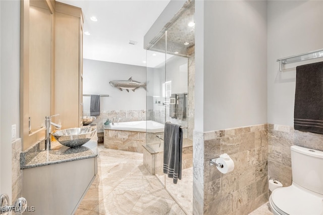 bathroom featuring tile walls, vanity, a relaxing tiled tub, and toilet