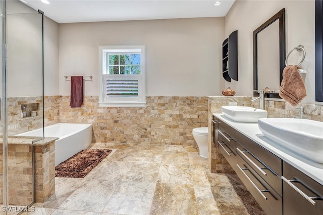 bathroom featuring vanity, toilet, tile walls, and a bath