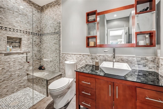 bathroom with toilet, vanity, tile walls, and a shower with door