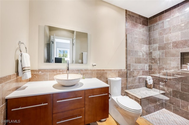 bathroom featuring toilet, vanity, a tile shower, and tile walls