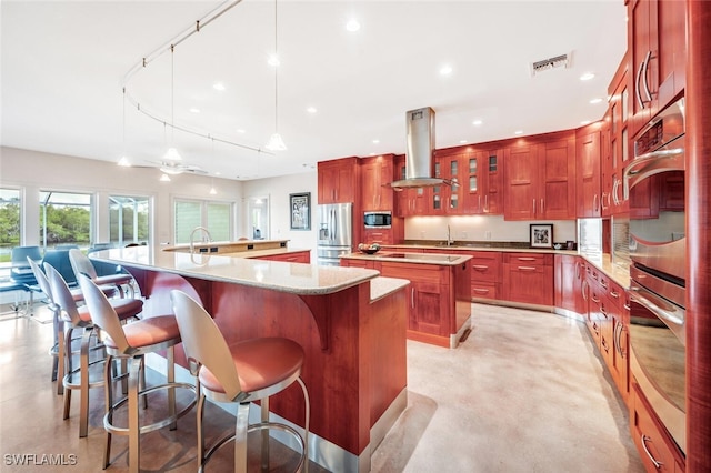 kitchen with appliances with stainless steel finishes, a kitchen island, decorative light fixtures, light stone counters, and exhaust hood