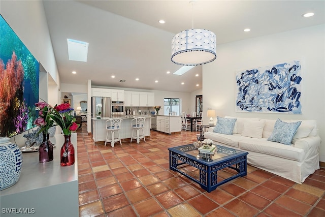 tiled living room with lofted ceiling with skylight and sink