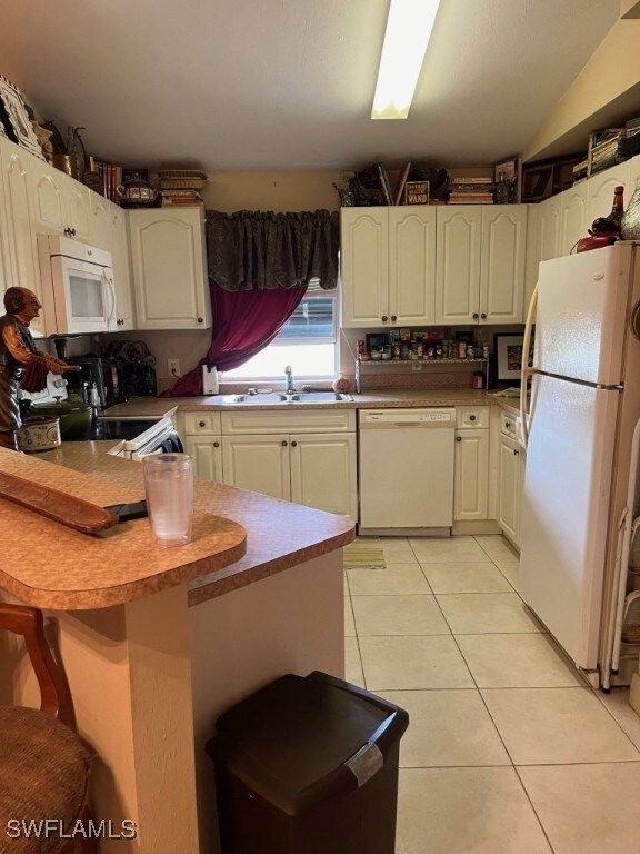 kitchen with kitchen peninsula, a breakfast bar area, light tile patterned flooring, sink, and white appliances