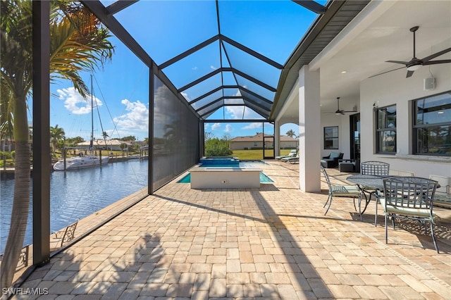 view of patio / terrace featuring ceiling fan, a water view, and glass enclosure