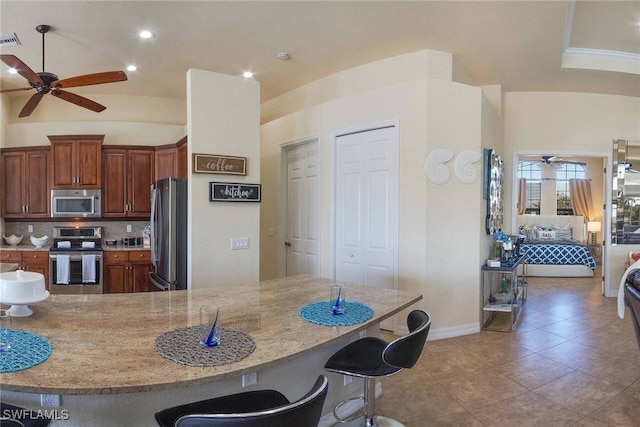 kitchen with tasteful backsplash, ceiling fan, a breakfast bar, stainless steel appliances, and tile patterned flooring