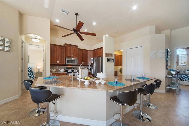 kitchen featuring light stone counters, light tile patterned floors, a spacious island, a breakfast bar area, and stainless steel appliances