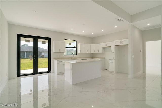 kitchen with sink, a kitchen island, white cabinets, and french doors