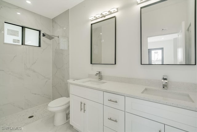 bathroom with toilet, vanity, a tile shower, and a wealth of natural light