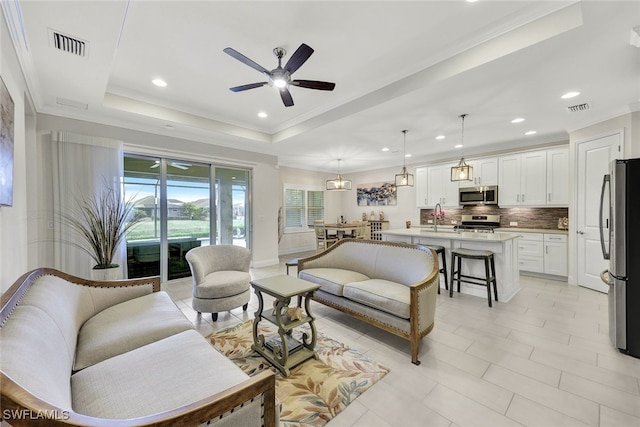 living room with ceiling fan, ornamental molding, sink, and a tray ceiling