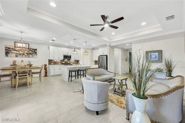 living room with a tray ceiling, crown molding, light tile patterned flooring, and ceiling fan with notable chandelier