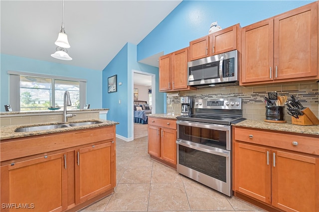 kitchen featuring lofted ceiling, light stone counters, appliances with stainless steel finishes, pendant lighting, and sink