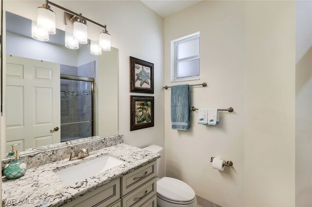 bathroom featuring a shower with door, vanity, and toilet