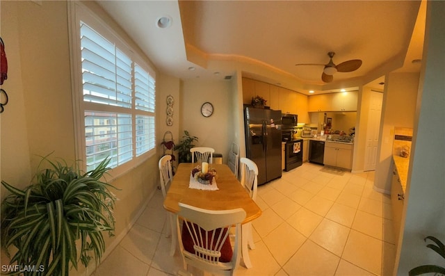 tiled dining area with ceiling fan and a tray ceiling