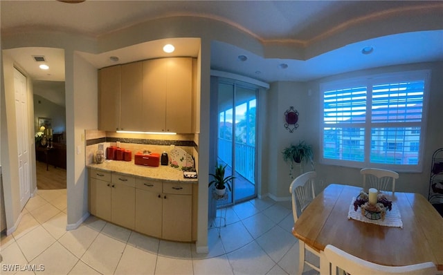 kitchen with cream cabinetry, light tile patterned floors, backsplash, and light stone countertops