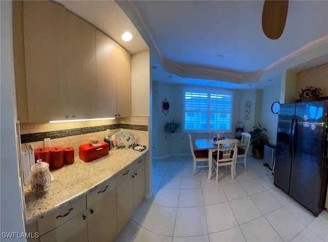 kitchen featuring light stone countertops, tasteful backsplash, a raised ceiling, light tile patterned floors, and fridge with ice dispenser