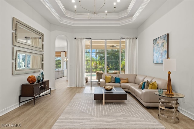 living room with a wealth of natural light, a raised ceiling, light wood-type flooring, and ornamental molding