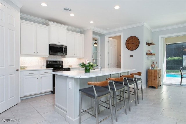 kitchen featuring stainless steel microwave, backsplash, a kitchen island with sink, and light countertops