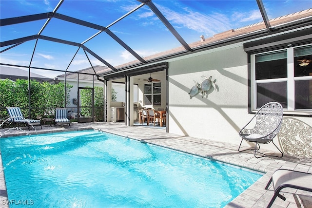 outdoor pool with glass enclosure, a ceiling fan, and a patio area