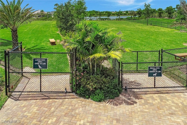 view of gate with a water view, a lawn, and fence