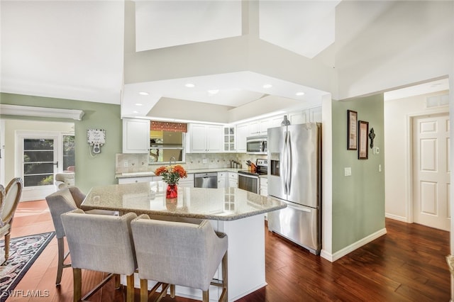 kitchen featuring decorative backsplash, light stone counters, stainless steel appliances, white cabinets, and dark hardwood / wood-style floors