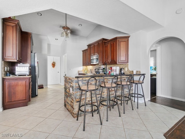 kitchen featuring kitchen peninsula, ceiling fan, appliances with stainless steel finishes, backsplash, and a kitchen bar