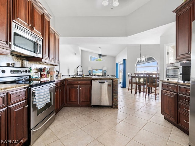 kitchen featuring sink, light tile patterned flooring, ceiling fan with notable chandelier, stainless steel appliances, and vaulted ceiling