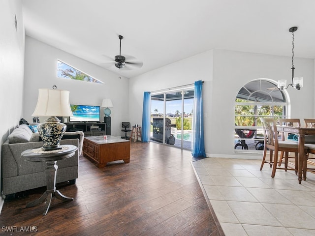 living room with a wealth of natural light, vaulted ceiling, wood-type flooring, and ceiling fan with notable chandelier