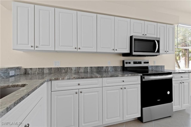 kitchen with white cabinets, appliances with stainless steel finishes, light tile patterned flooring, and stone counters