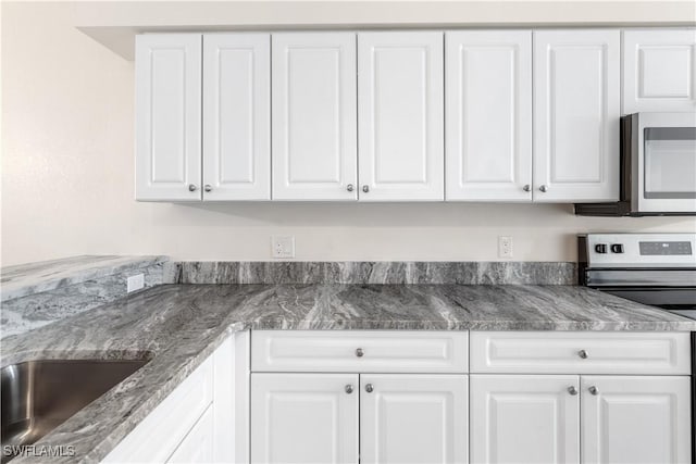 kitchen with appliances with stainless steel finishes, sink, stone countertops, and white cabinetry