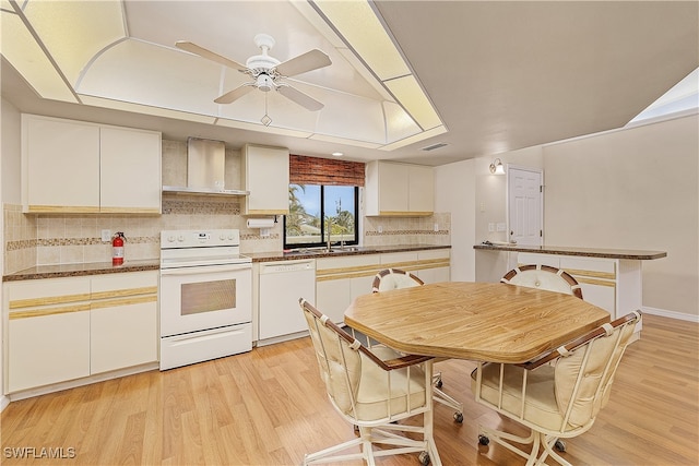 kitchen with white cabinetry, tasteful backsplash, wall chimney exhaust hood, white appliances, and light hardwood / wood-style flooring