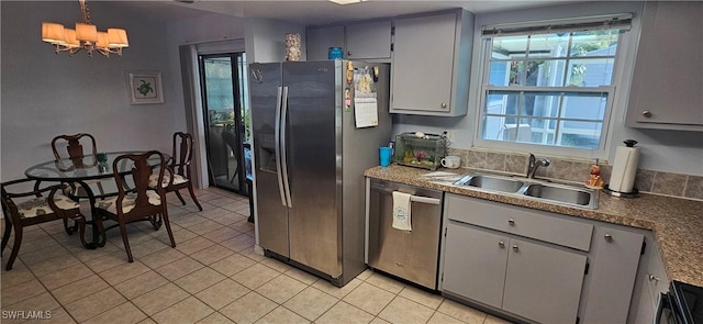 kitchen with sink, gray cabinets, light tile patterned floors, stainless steel appliances, and a chandelier