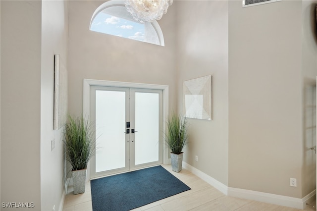 tiled entrance foyer with french doors, a towering ceiling, and a chandelier