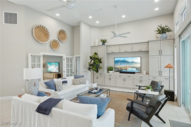 living room featuring a towering ceiling, ceiling fan, and light hardwood / wood-style floors