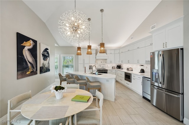 kitchen with white cabinetry, stainless steel appliances, decorative light fixtures, a breakfast bar area, and a kitchen island with sink