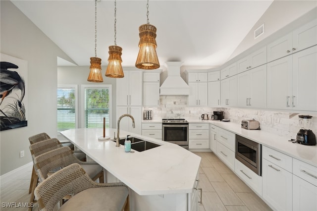 kitchen with an island with sink, appliances with stainless steel finishes, premium range hood, vaulted ceiling, and pendant lighting