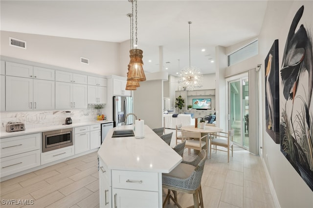 kitchen featuring appliances with stainless steel finishes, an island with sink, hanging light fixtures, and white cabinets