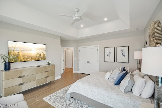 bedroom with a closet, a raised ceiling, light wood-type flooring, and ceiling fan