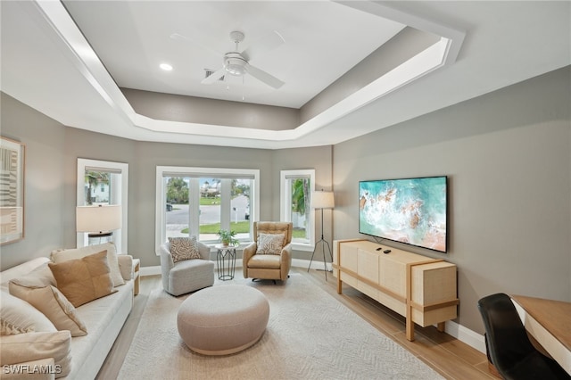 living room featuring light hardwood / wood-style floors, a tray ceiling, and ceiling fan