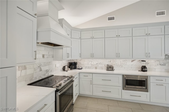 kitchen with white cabinets, tasteful backsplash, appliances with stainless steel finishes, premium range hood, and vaulted ceiling